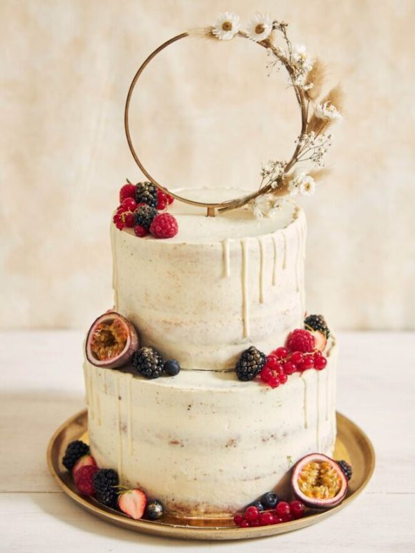 A vertical shot of a wedding cake decorated with fresh fruits and berries and a flower ring